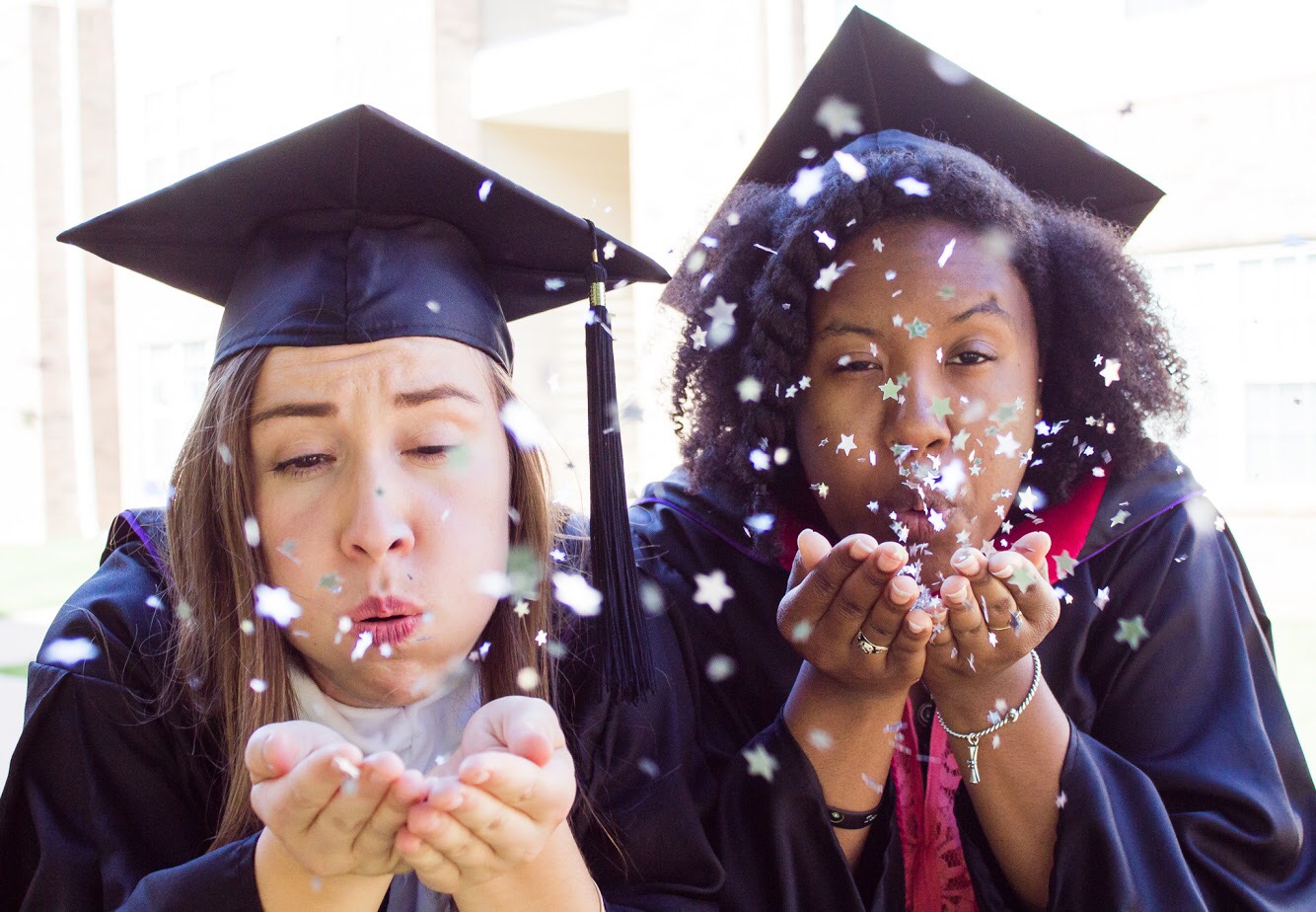 Two graduates blowing confetti in celebration